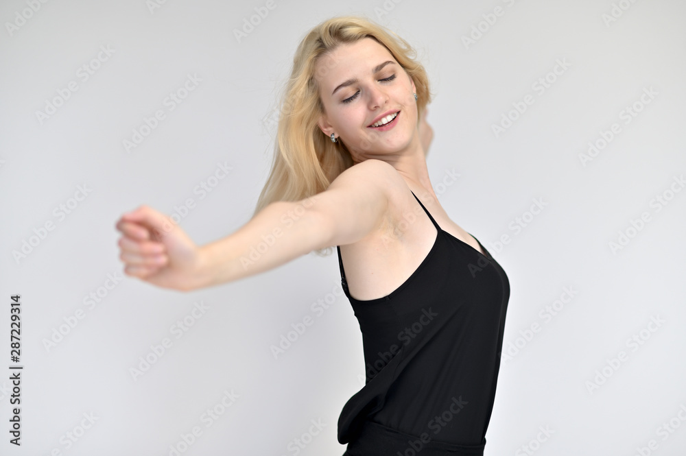 Portrait of a cute blonde student girl, a young woman in a black dress with beautiful curly hair on a white background in different poses. Shows hands to the sides. Beauty, brightness, emotions. Portrait of a cute blonde student girl, a young woman in a black dress with beautiful curly hair on a white background in different poses. Shows hands to the sides. Beauty, brightness, emotions.