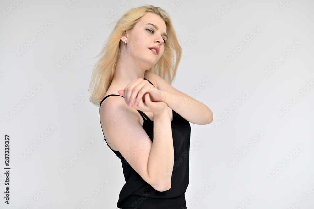 Portrait of a cute blonde student girl, a young woman in a black dress with beautiful curly hair on a white background in different poses. Shows hands to the sides. Beauty, brightness, emotions. Portrait of a cute blonde student girl, a young woman in a black dress with beautiful curly hair on a white background in different poses. Shows hands to the sides. Beauty, brightness, emotions.