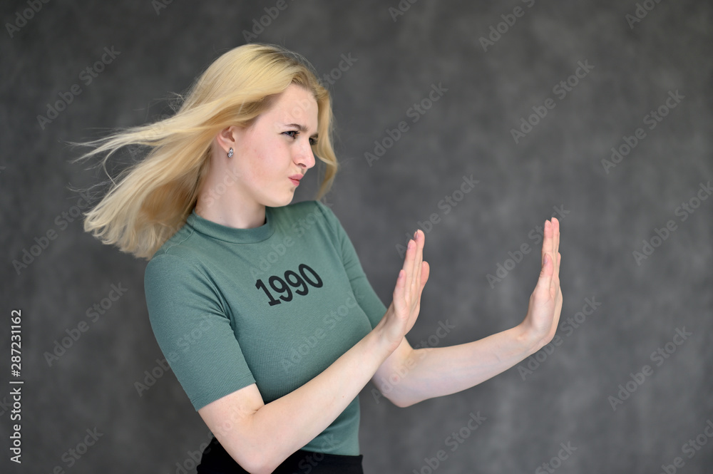 Portrait of a cute blonde student girl, a young woman in a green T-shirt with beautiful curly hair on a gray background in different poses. Shows hands to the sides. Beauty, brightness, emotions. Portrait of a cute blonde student girl, a young woman in a green T-shirt with beautiful curly hair on a gray background in different poses. Shows hands to the sides. Beauty, brightness, emotions.