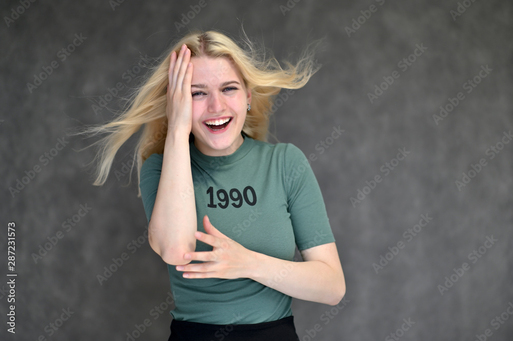 Portrait of a cute blonde student girl, a young woman in a green T-shirt with beautiful curly hair on a gray background in different poses. Shows hands to the sides. Beauty, brightness, emotions. Portrait of a cute blonde student girl, a young woman in a green T-shirt with beautiful curly hair on a gray background in different poses. Shows hands to the sides. Beauty, brightness, emotions.