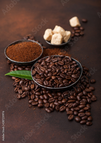 Fresh raw organic coffee beans with ground powder and cane sugar cubes with coffee trea leaf on brown background.