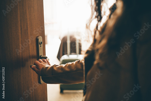 Woman opening door and entering in hotel apartment. Detail female hand in silhouette holding door handle moving inside room through dark hall. Concept of comfortable vacation photo