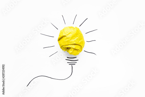 Business ideas. Composition of modern crumpled yellow paper ball and drawing of lamp bulb on white background. Creative and startup concepts.