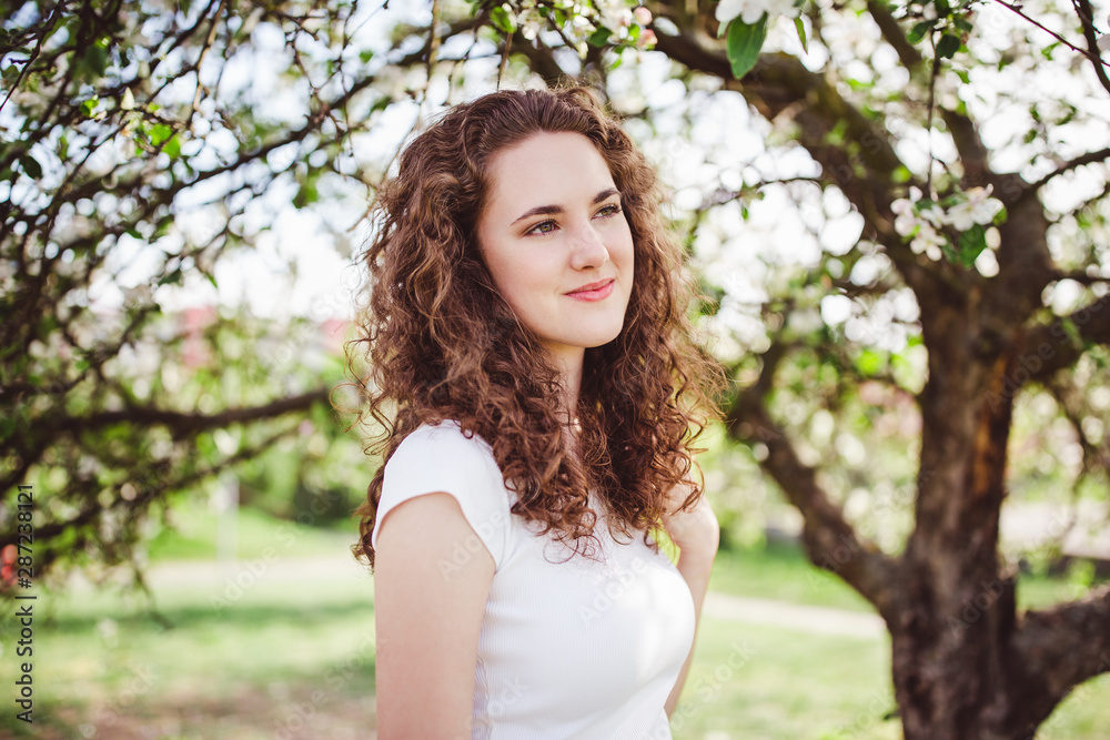 Cheerful young woman in a white t-shirt under the blooming tree.