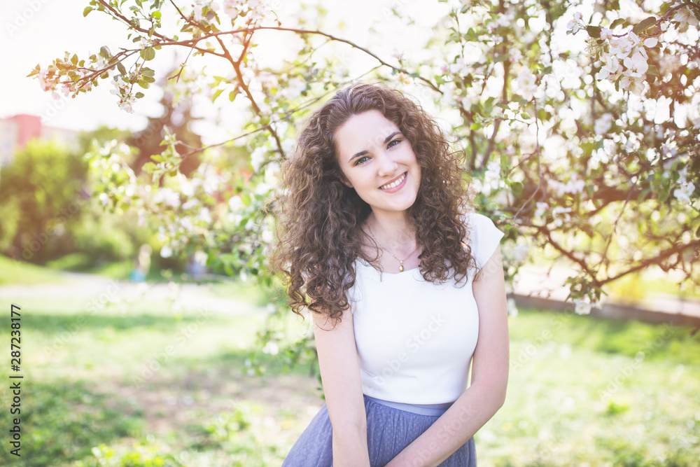 Cheerful young woman in a white t-shirt under the blooming tree.