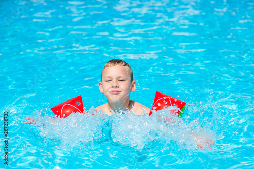 Happy kid boy having fun in an swimming pool. Active happy healthy preschool child learning to swim. With safe floaties or swimmies.