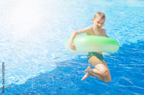 happy boy with green inflatable jumping in the pool. Summer day