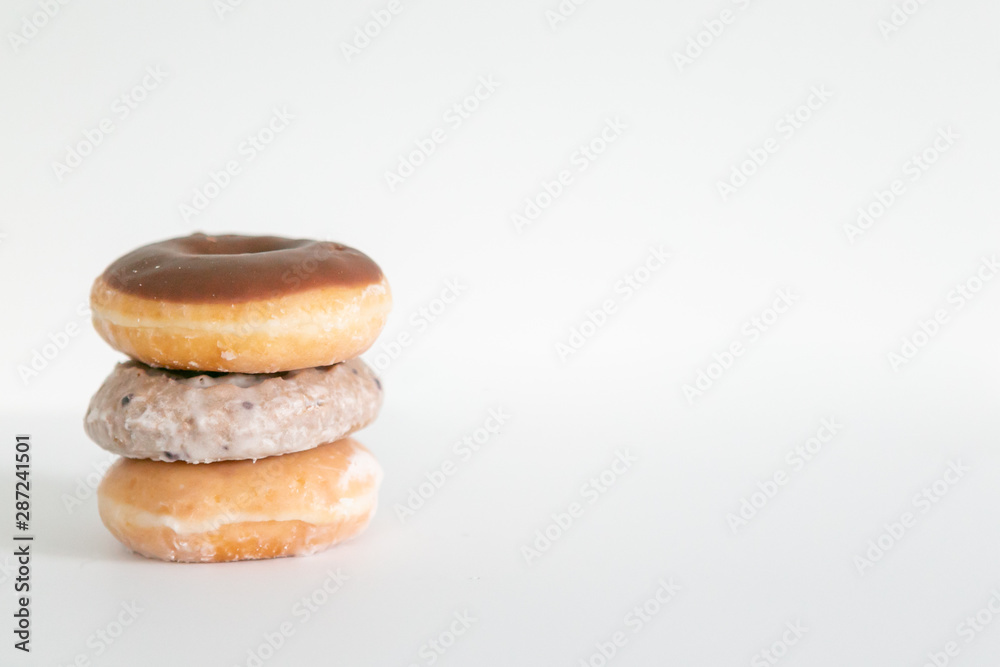 Three donuts stacked on one another, chocolate iced, blueberry cake, and plain glaze, white background, copy space Three donuts stacked on one another, chocolate iced, blueberry cake, and plain glaze, white background, copy space