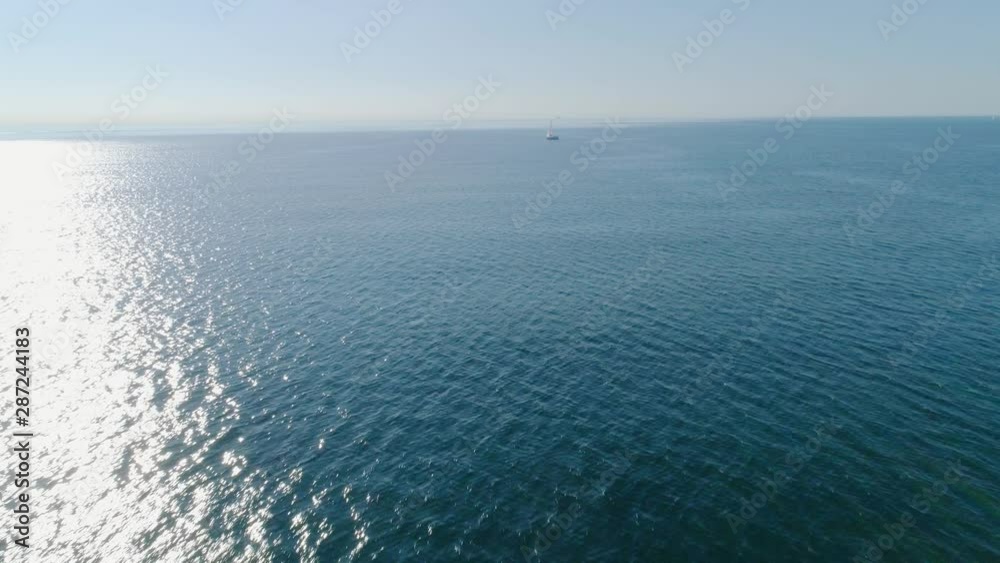 Forward flight over calm ocean bay water towards white sailboat on thte horizon Forward flight over calm ocean bay water towards white sailboat on thte horizon