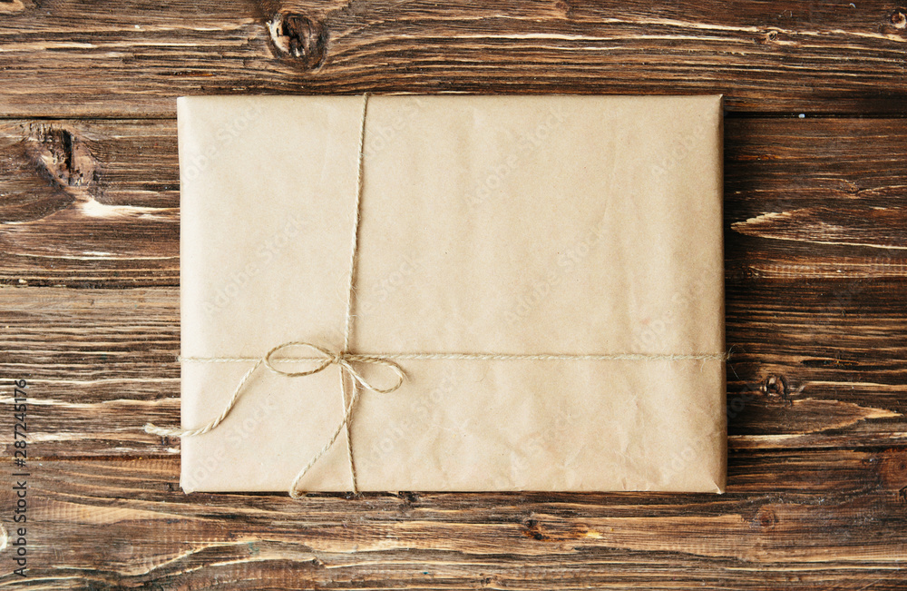 Overhead view of a single holiday package wrapped with eco friendly craft paper and tied with twine. Square format on a rustic wooden table. Overhead view of a single holiday package wrapped with eco friendly craft paper and tied with twine. Square format on a rustic wooden table.