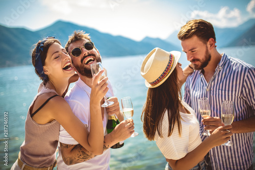 Young attractive and trendy people standing over the sea and drinking champagne while smiling broadly. © Mediteraneo