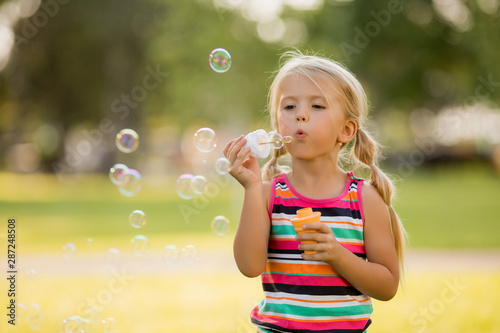 little blonde girl inflates soap bubbles in summer on a walk   International children s day