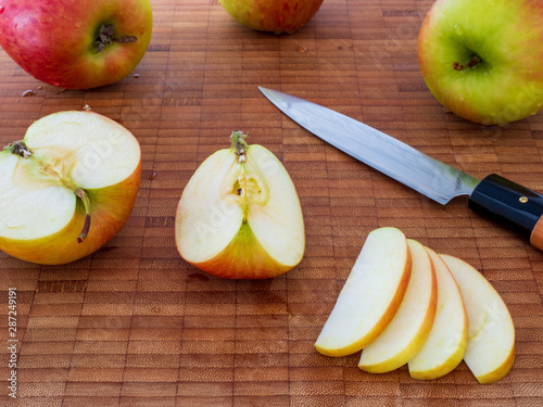 Mehrere Äpfel mit geschnittenen Apfelstücken und Apfelscheiben mit Messer auf Holzbrett