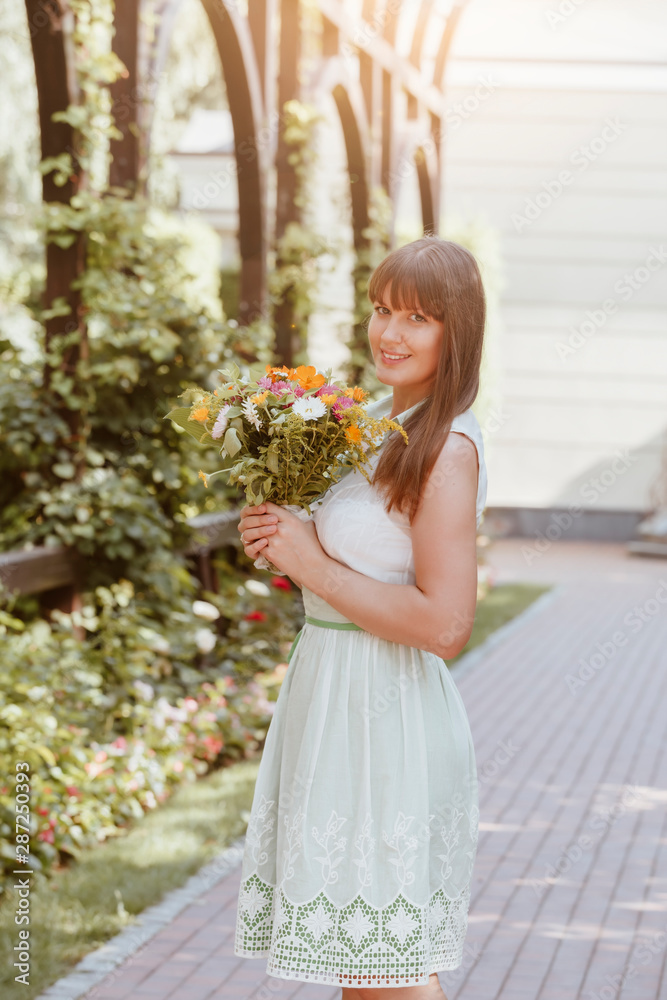 Beautiful girl in a summer dress with a bouquet in her hands in the park. Portrait of a beautiful brown-haired woman in the summer with flowers. Bride Beautiful girl in a summer dress with a bouquet in her hands in the park. Portrait of a beautiful brown-haired woman in the summer with flowers. Bride