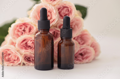 Dark cosmetic bottles, with pink roses on a whait background. Copy space. Friendly natural cosmetics concept. Minimalism. Beauty blogger, spa salon, terapy salon. photo