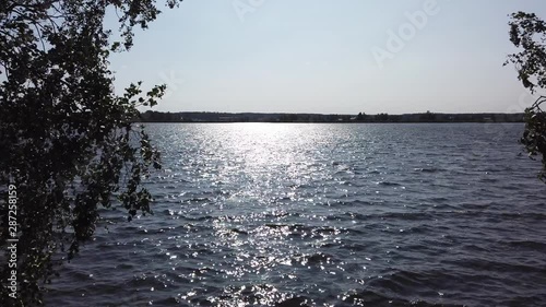 Lake on summer day. Reflection of sunlight on water surface in Sastamala, Finland. Trees swing in the wind. photo