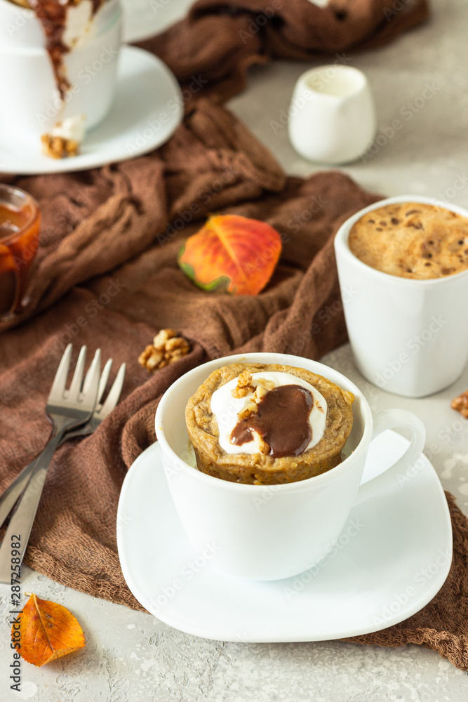 Carrot op pumpkin mug cupcake with whipped cream, caramel sauce and walnuts in a white ceramic mug. Cozy autumn or winter breakfast. Healthy dessert. Carrot op pumpkin mug cupcake with whipped cream, caramel sauce and walnuts in a white ceramic mug. Cozy autumn or winter breakfast. Healthy dessert.