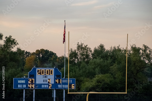 Football end zone with goal posts, Amercian flag and score board during evening sunset at local high school