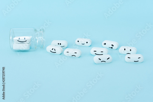  Pills with funny faces and a glass bottle on a blue background. Pharmacy antibiotic. Treating with antidepressant. Mental disorder. The concept of antidepressants and healing. Copy space.