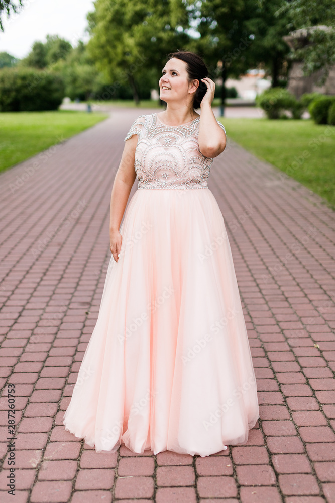 Brunette caucasian model in elegant floor-length pink dress dreamy looking away in park. Brunette caucasian model in elegant floor-length pink dress dreamy looking away in park.
