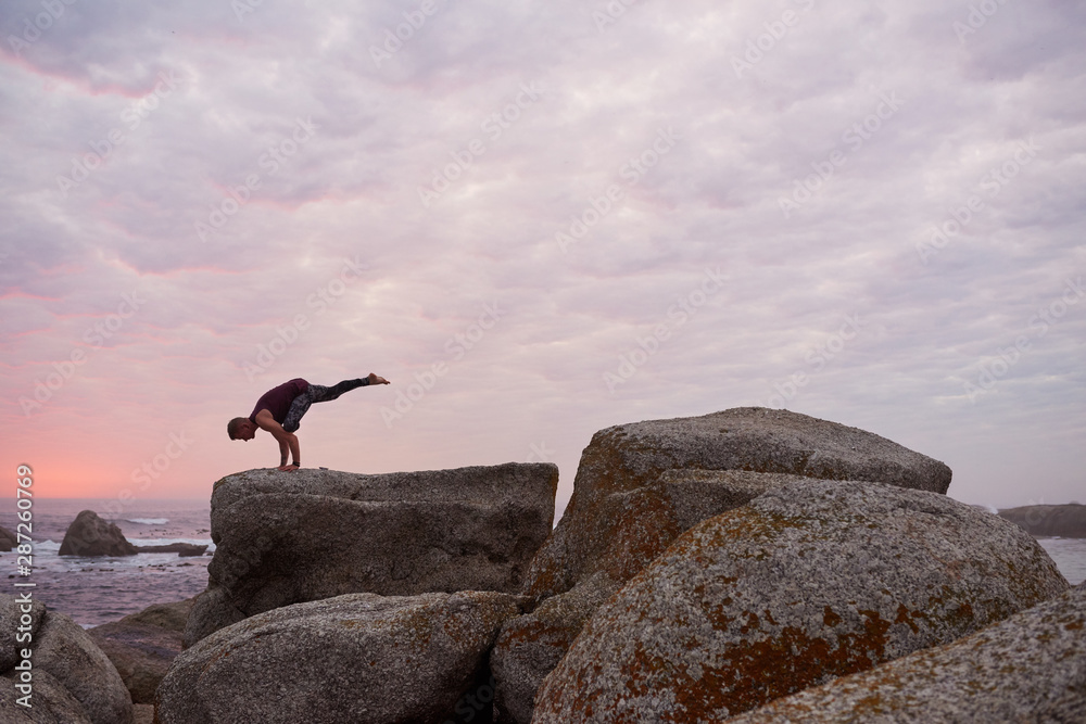 Man doing the one legged crow pose by the ocean Man doing the one legged crow pose by the ocean