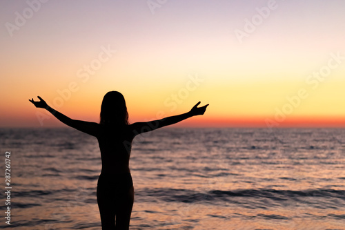 Silhouette of beautiful young gracile pensive woman with a freedom feeling  rise hand up on beautiful sunset. Freedom and travel adventure happy feeling concept. © Juliaap