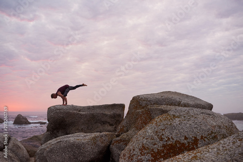 Man doing the one legged crow pose by the ocean