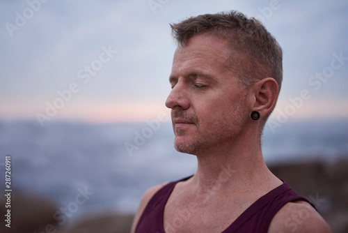 Man standing by the ocean and meditating at dusk