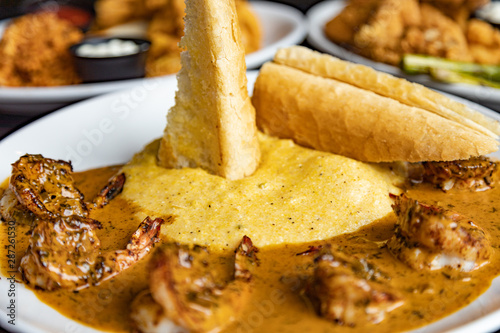 Crispy bread stuck in the grits and shrimp creole cuisine on a white plate. Close up with other platters blurred in the background
