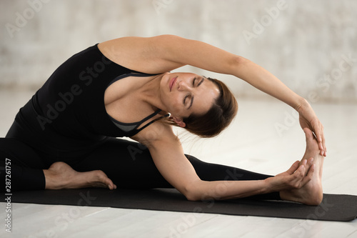 Young woman practicing yoga, doing Janu Sirsasana exercise close up