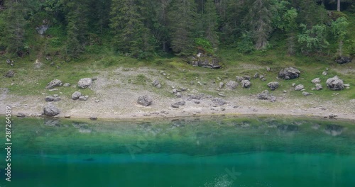 Shore of Lake Carezza, mountain lake famous for the dark green color and the beautiful panorama of mountains in the background. Reflection of the stones and trees in the Lake. South Tirol, Italy photo