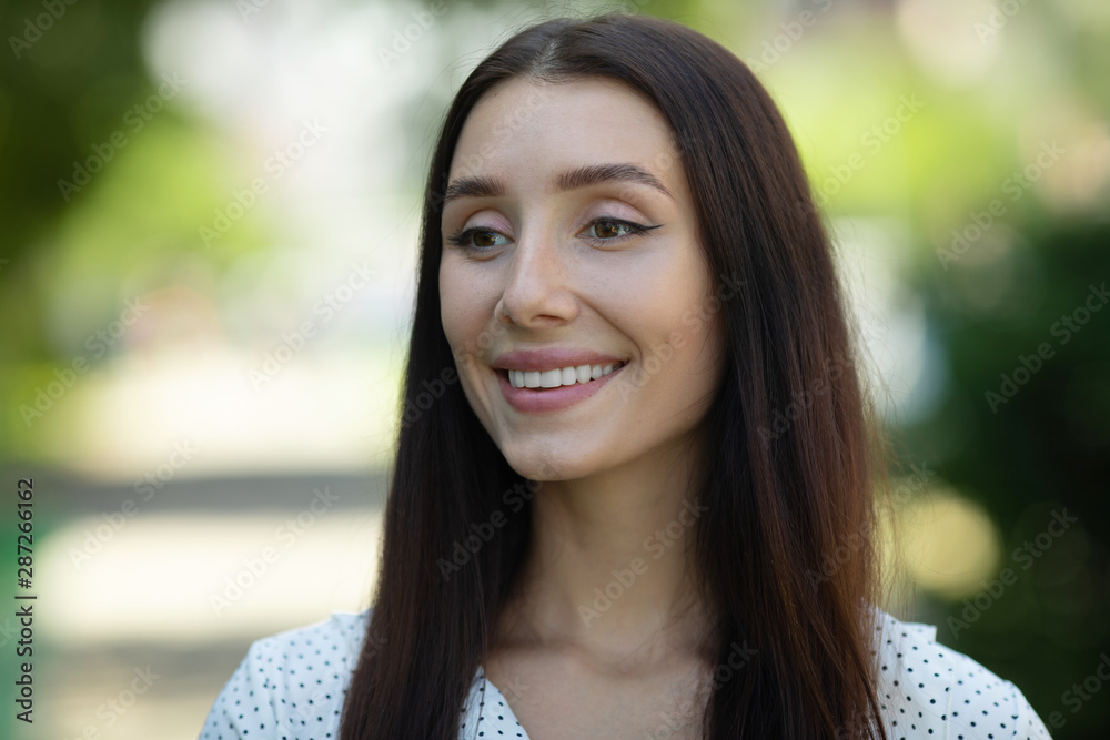 Close up portrait of a beautiful smiling girl with brown hair wearing summer dress and looking at camera outdoors