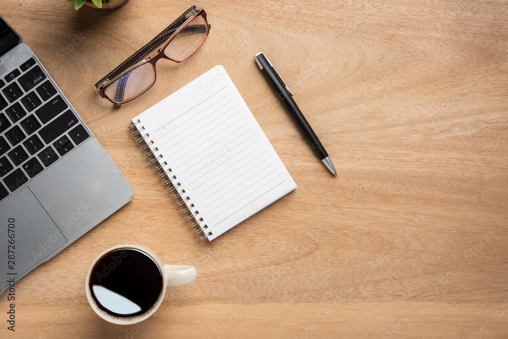 Wooden office desk table with blank notebook, laptop computer, cup of black coffee and supplies. Top view with copy space, flat lay. Wooden office desk table with blank notebook, laptop computer, cup of black coffee and supplies. Top view with copy space, flat lay.