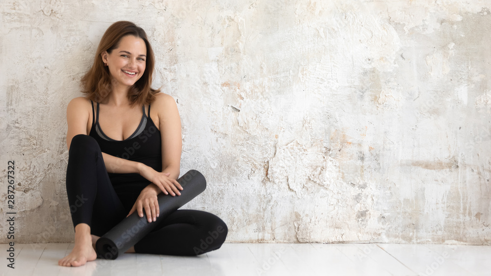 Happy smiling woman holding black yoga mat, sitting on floor