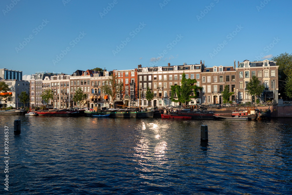Urban city view of Amsterdam canal with mobile water living boats at sunset