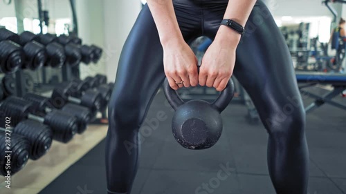 Sporty female lifting kettlebell. Athlete woman wearing black leggings and trainers training with hard weight in sports club. Close-up. photo