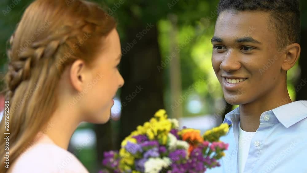 Male teen giving flowers to cute girl in park, declaration of love, magic moment Male teen giving flowers to cute girl in park, declaration of love, magic moment