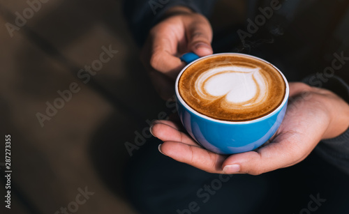 Female barista hands holding cup of fresh delicious cappuccino with latte art cream foam, brewed and made with love and take care concept, good service coffee shop