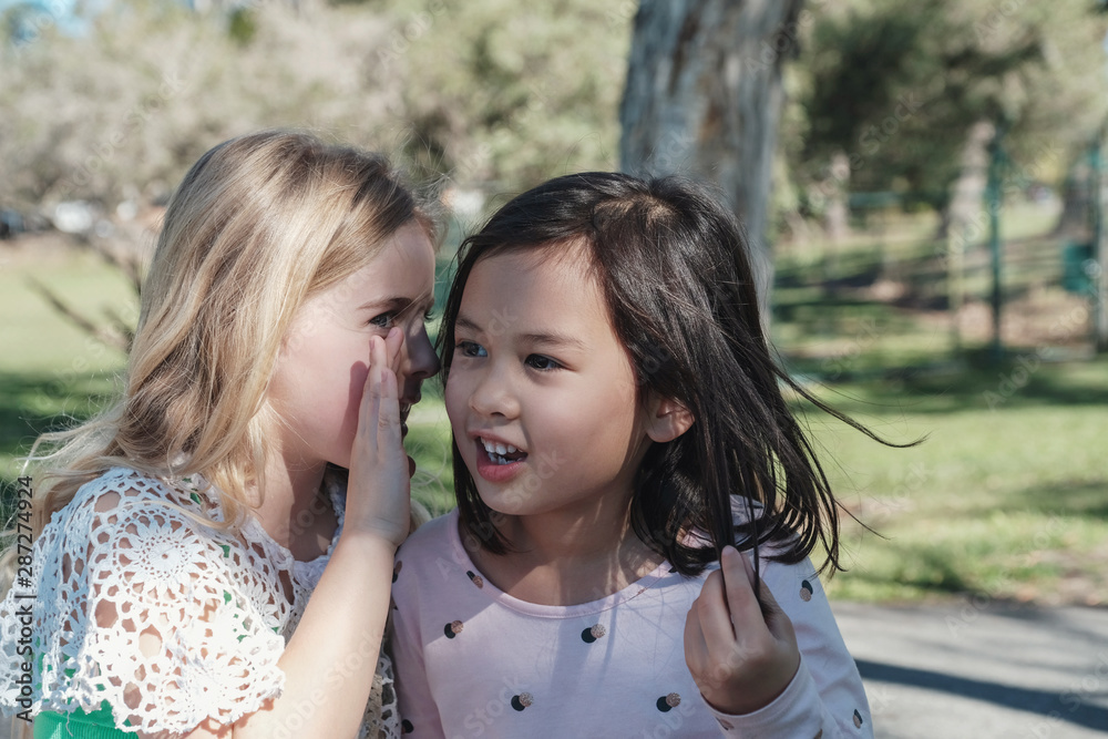 multiethnic young little girls playing kids Chinese whispering  in the park, best friends and positive friendship concept