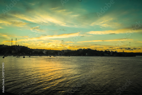 Sunset at Ponta do Xaréu, Itacaré, Bahia, with tranquil river waters reflecting the vibrant orange sky and silhouetted figures. A peaceful and serene moment capturing nature's beauty