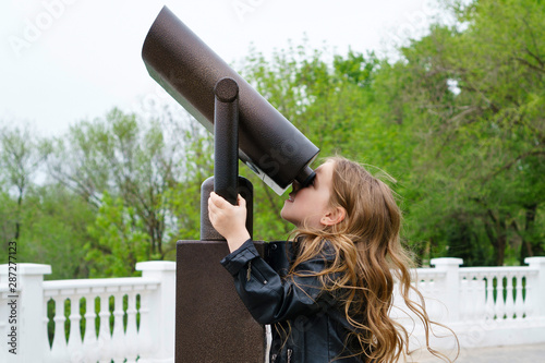 Fashionable little schoolgirl looking through stationary binoculars. The concept of learning and new knowledge. Close-up photo