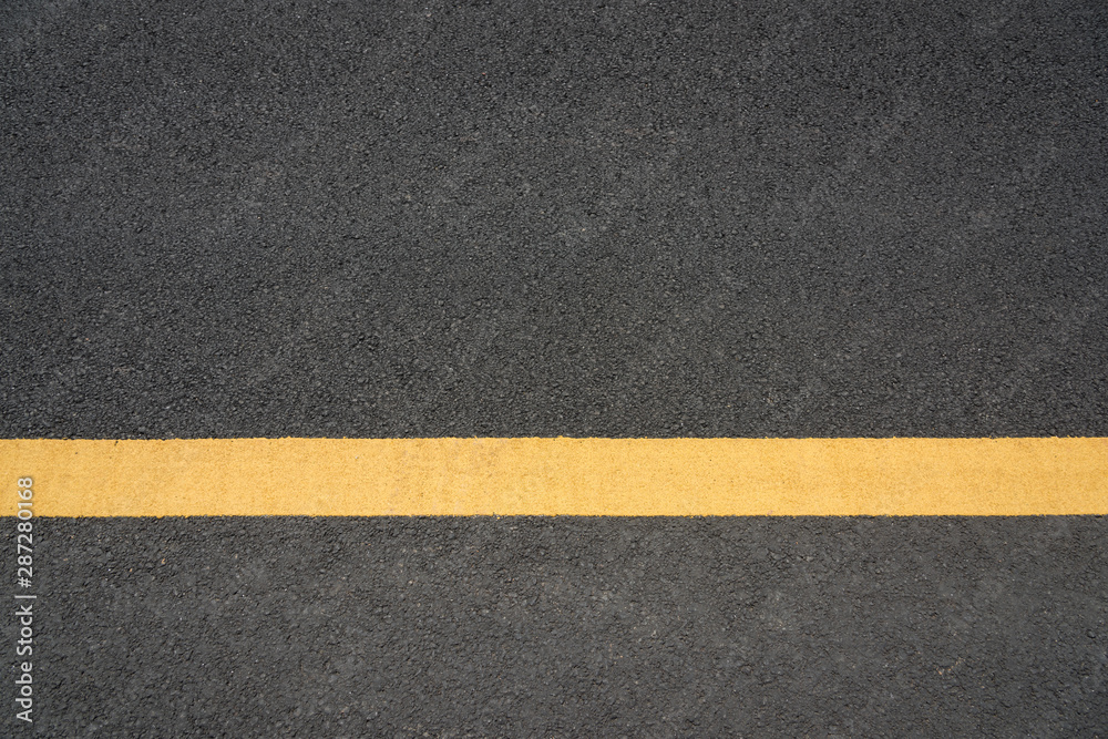 Fototapeta premium A parallel yellow paint line close-up text space on black asphalt road