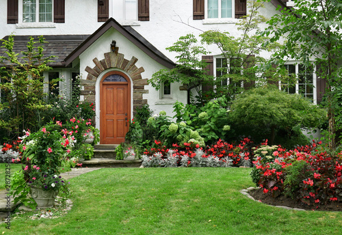 Fényképezés stucco house with wooden front door and flowers in front yard