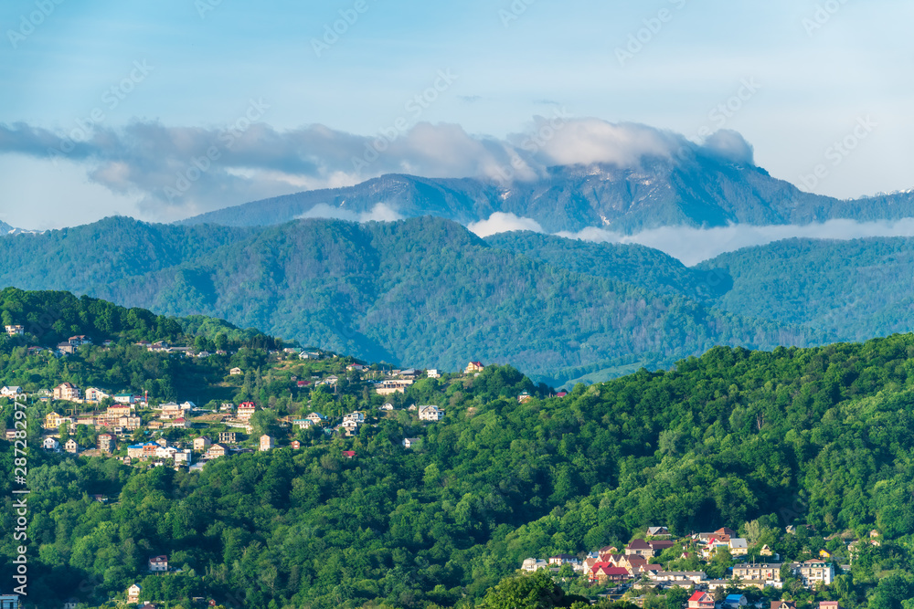 View on a green hilly valley with houses and high snowy mountains on the horizon.