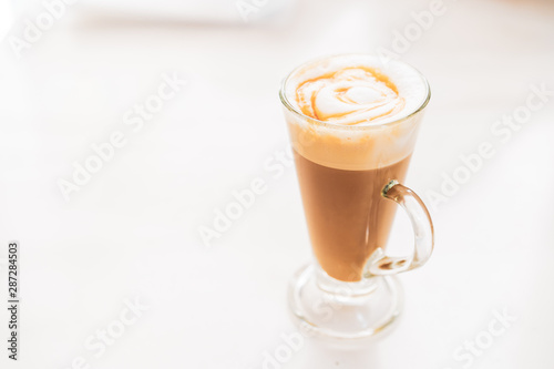 Hot caramel macchiato in a tall glass with caramel sauce on top close up.