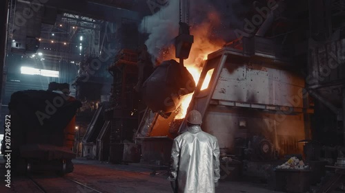 Iron foundry. The steelmaker of the converter shop manages the pouring of steel into the furnace. Cast iron is pouring from a ladle. And the stove leaves thick smoke.