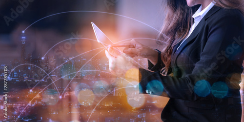 Double exposure of businesswoman using digital tablet with city scape and network connection diagram