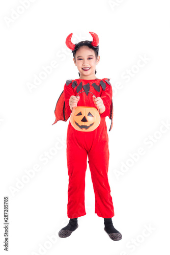 Full length of little asian girl in red devil costume standing and holding halloween pumpkin bucket over white background