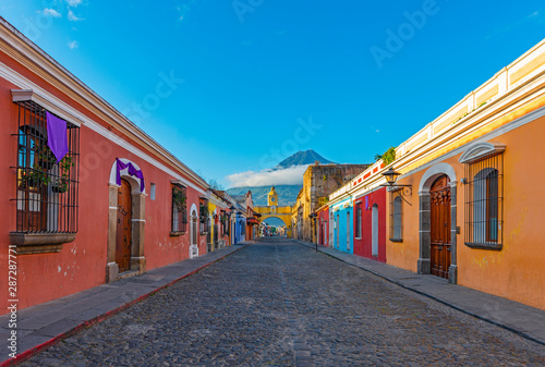 Foto Cityscape of the colorful main street of Antigua city at sunrise with the famous yellow arch and the Agua volcano in the background, Guatemala, Central America