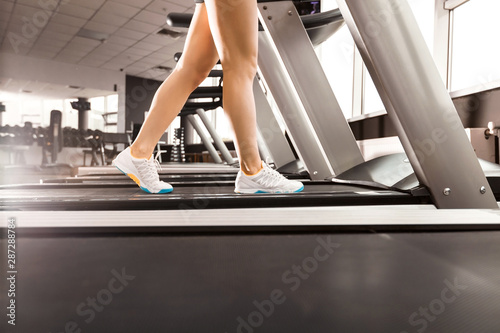 close up womans legs walking at the treadmill in the gym over sunrise. wearing in white orange blue sneakers. Cardio exercise